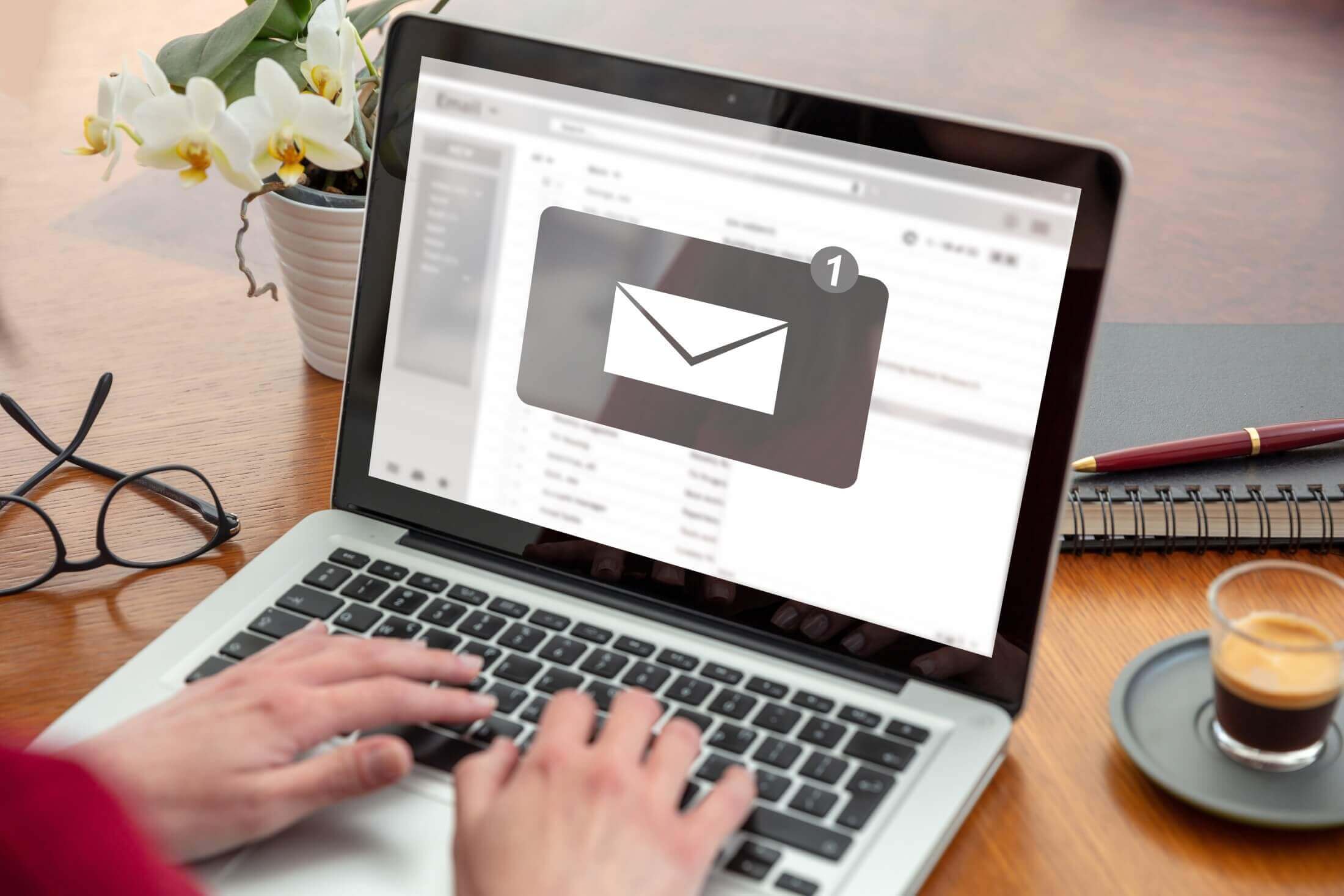 A woman's hands typing on a laptop with an email notification icon on the screen, indicating the reception of a new message.